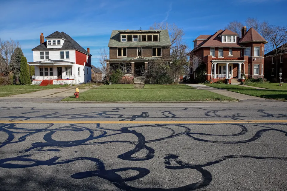 Three two-story houses on residential street in Detroit, Michigan. Center house appears abandoned.